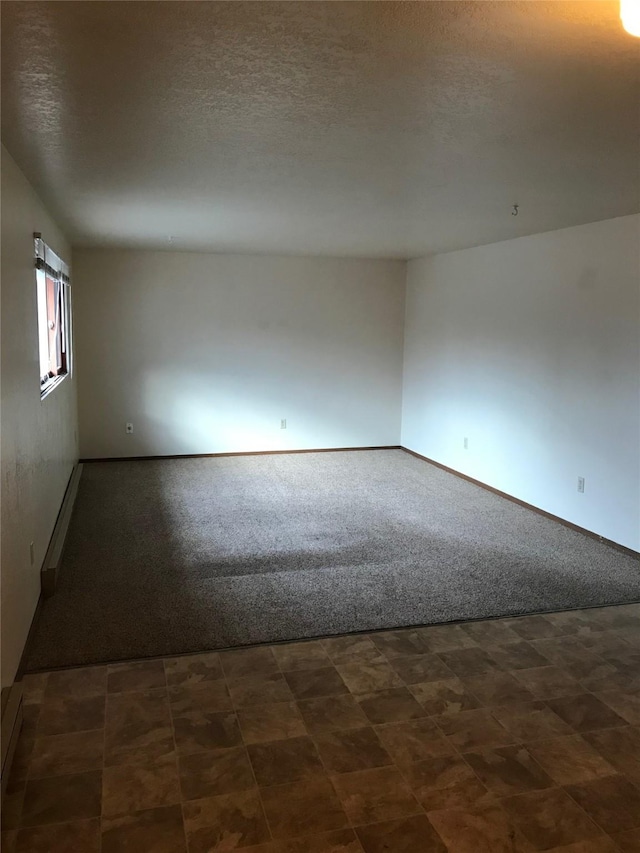 spare room featuring a textured ceiling and dark colored carpet