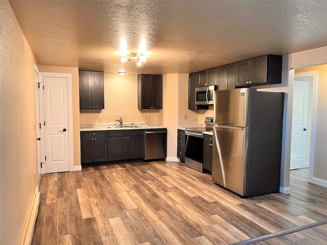 kitchen featuring a textured ceiling, dark brown cabinetry, appliances with stainless steel finishes, a baseboard heating unit, and light hardwood / wood-style floors