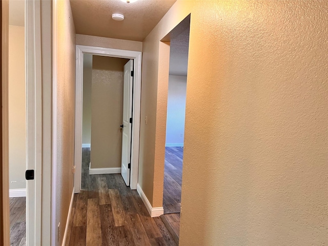 corridor with a textured ceiling and dark hardwood / wood-style floors