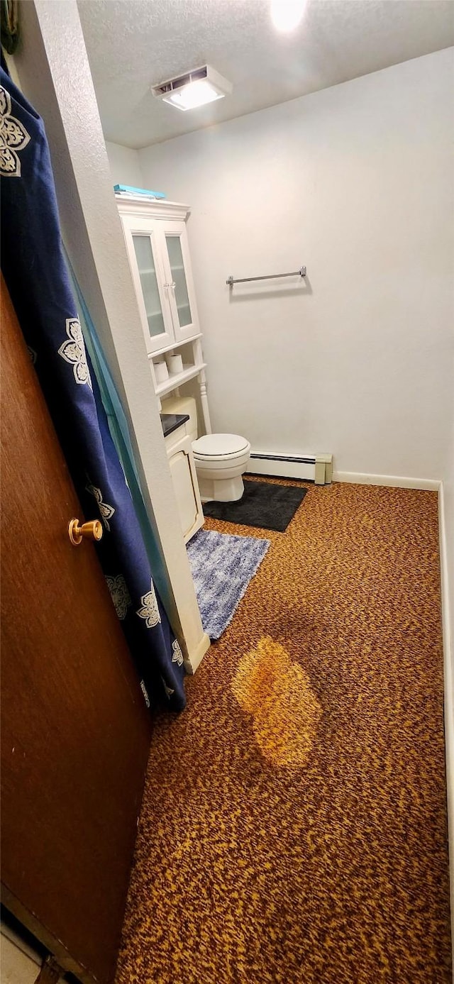 bathroom featuring a textured ceiling, a baseboard heating unit, and toilet