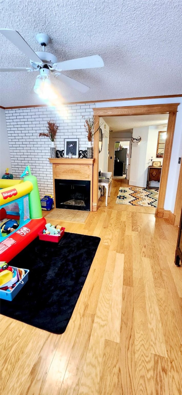 interior space with ceiling fan, a textured ceiling, wood-type flooring, and a fireplace