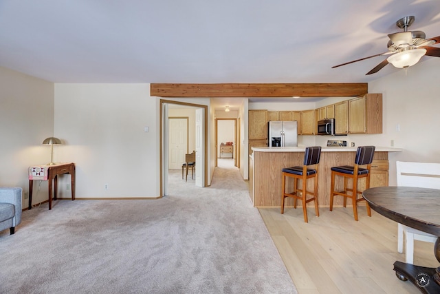 kitchen with light brown cabinets, stainless steel appliances, kitchen peninsula, ceiling fan, and beam ceiling