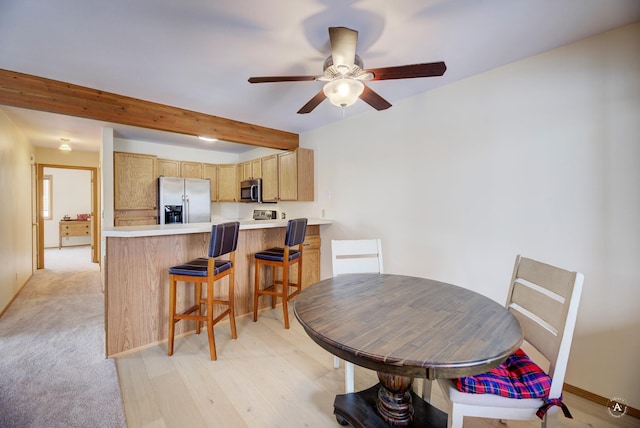 dining room featuring ceiling fan, light carpet, and beam ceiling