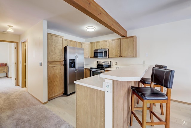 kitchen featuring light brown cabinets, stainless steel appliances, beamed ceiling, kitchen peninsula, and a breakfast bar