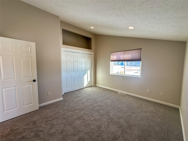 unfurnished bedroom with dark colored carpet, a textured ceiling, a closet, and vaulted ceiling