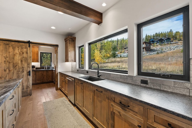 kitchen featuring a healthy amount of sunlight, sink, light wood-type flooring, beam ceiling, and a barn door