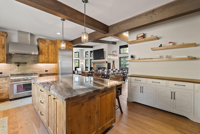 kitchen with a center island, wall chimney range hood, high end appliances, decorative backsplash, and hanging light fixtures