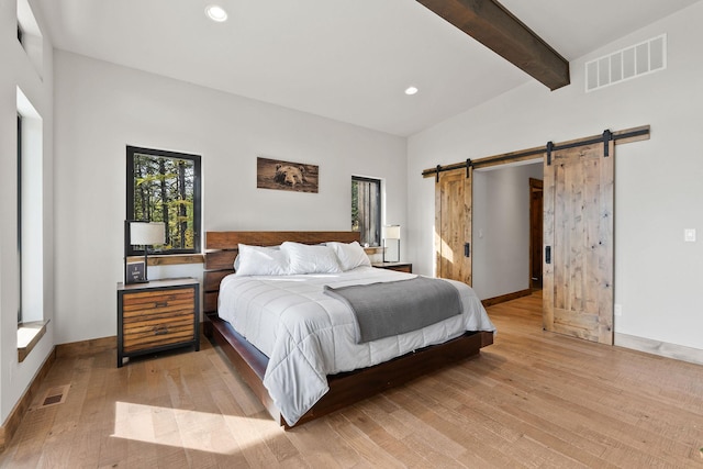 bedroom featuring beamed ceiling, a barn door, and light hardwood / wood-style floors