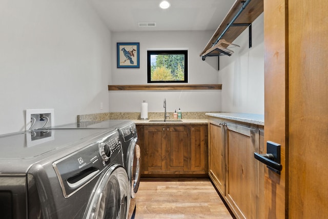 clothes washing area featuring cabinets, sink, light wood-type flooring, and washing machine and clothes dryer