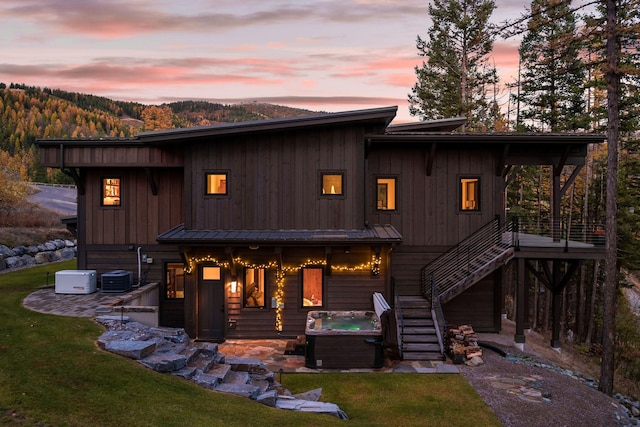 back house at dusk with a hot tub, a lawn, and a patio