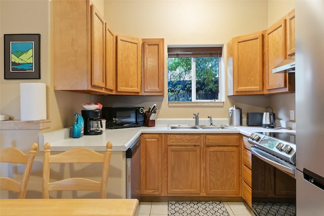 kitchen with light tile patterned flooring, under cabinet range hood, a sink, light countertops, and appliances with stainless steel finishes