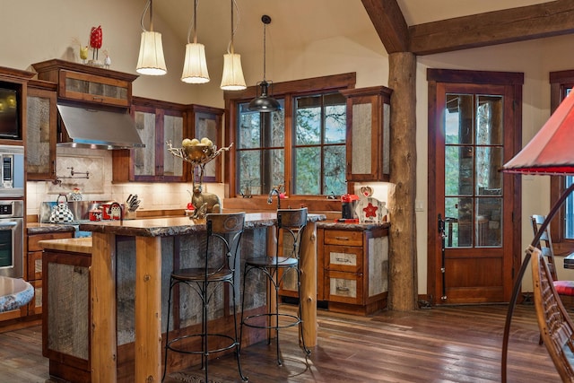 kitchen featuring hanging light fixtures, decorative backsplash, dark hardwood / wood-style floors, and wall chimney range hood