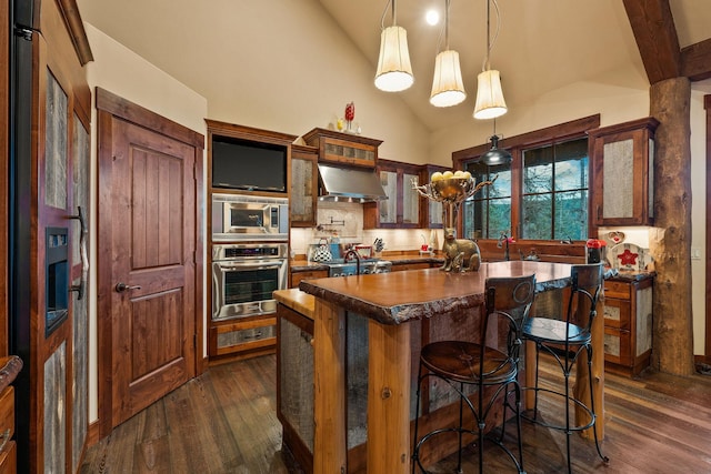 kitchen with appliances with stainless steel finishes, hanging light fixtures, decorative backsplash, a kitchen island, and wall chimney exhaust hood