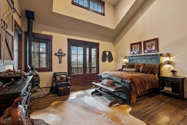 bedroom featuring dark wood-type flooring, a high ceiling, a wood stove, and french doors