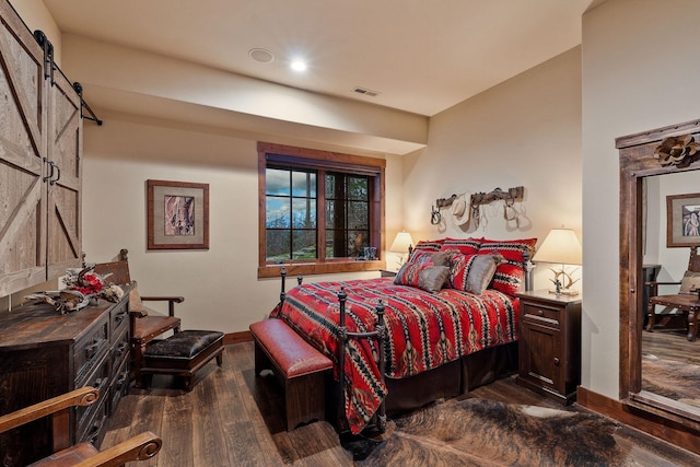 bedroom with a barn door and dark wood-type flooring