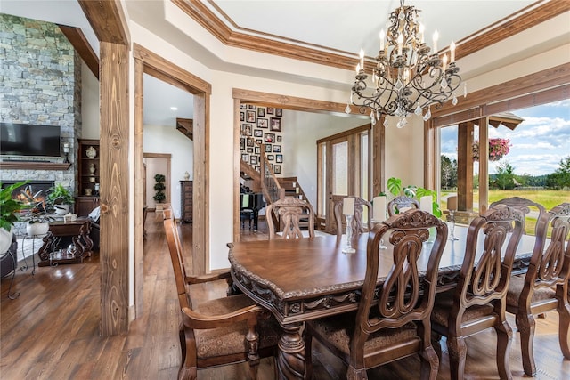 dining area with a stone fireplace, an inviting chandelier, dark hardwood / wood-style floors, and crown molding