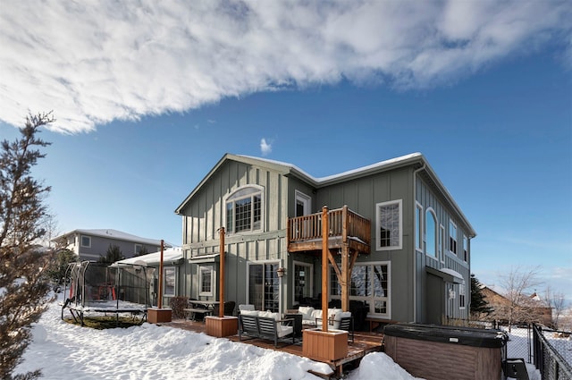 snow covered property featuring a balcony, a trampoline, and a hot tub