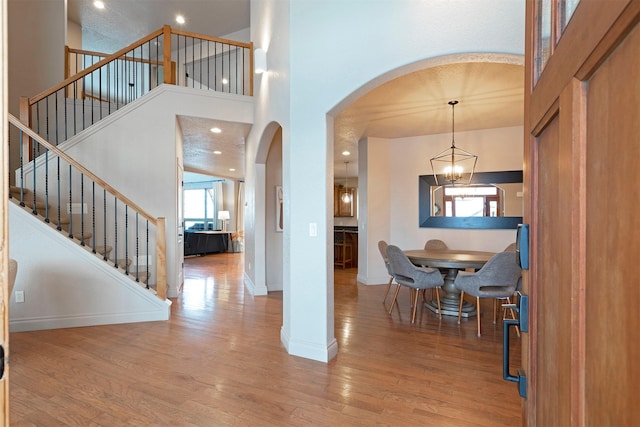 entryway with a towering ceiling, an inviting chandelier, and wood-type flooring