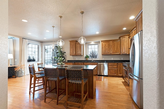 kitchen with a kitchen breakfast bar, decorative light fixtures, light wood-type flooring, plenty of natural light, and stainless steel appliances