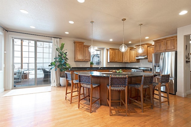 kitchen with pendant lighting, a kitchen island, stove, and stainless steel refrigerator with ice dispenser