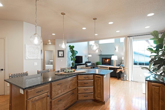 kitchen featuring a textured ceiling, a kitchen island, light hardwood / wood-style flooring, pendant lighting, and dark stone counters