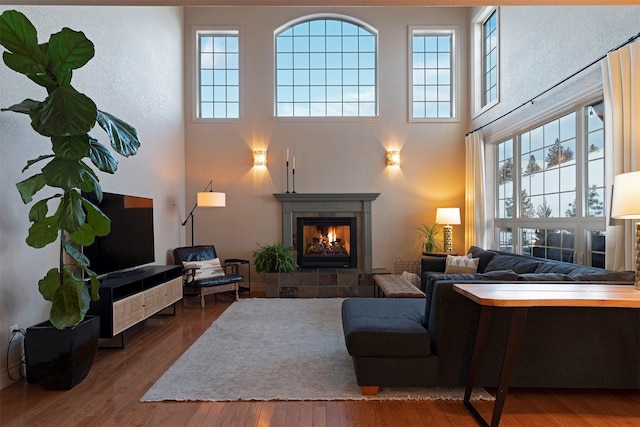 living room featuring hardwood / wood-style flooring, plenty of natural light, a tile fireplace, and a towering ceiling