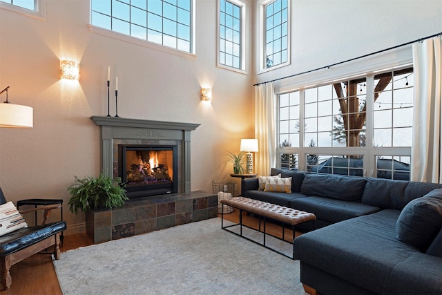 living room featuring a tiled fireplace, a healthy amount of sunlight, a high ceiling, and hardwood / wood-style floors