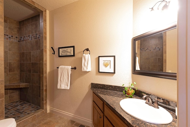 bathroom with a tile shower, toilet, tile patterned flooring, and vanity