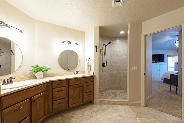 bathroom with a textured ceiling, tile patterned flooring, tiled shower, vanity, and ceiling fan