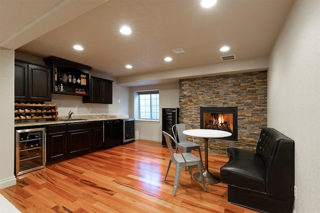 bar with light hardwood / wood-style floors, sink, beverage cooler, and black dishwasher