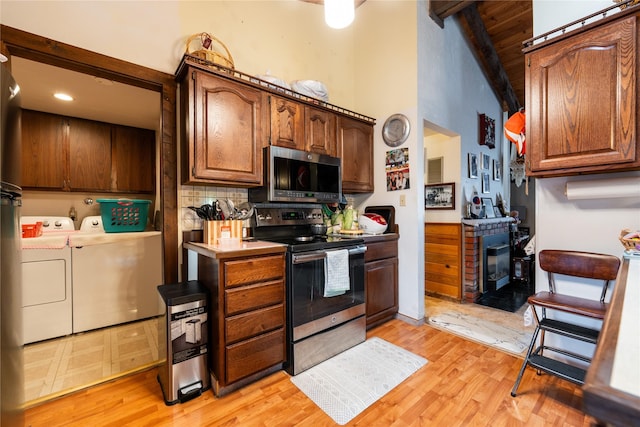 kitchen featuring appliances with stainless steel finishes, lofted ceiling with beams, tasteful backsplash, washer and dryer, and light hardwood / wood-style floors