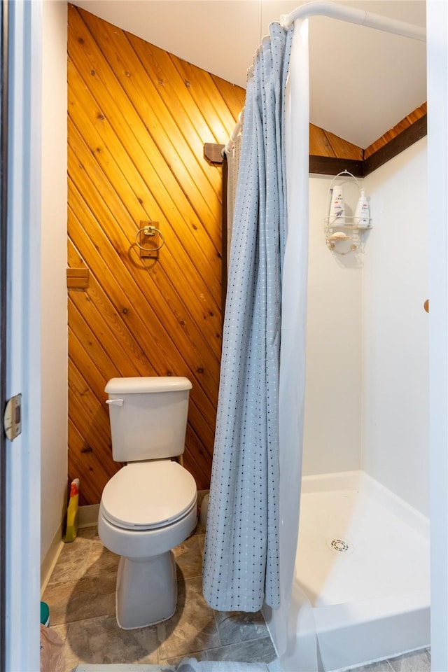 full bathroom with toilet, a stall shower, and wooden walls