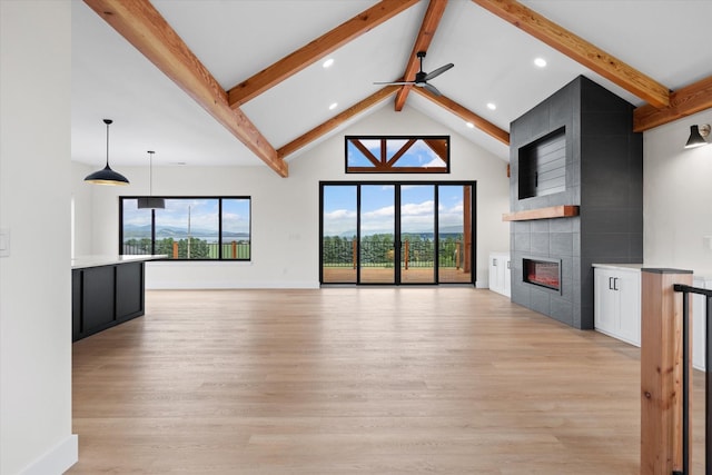 unfurnished living room featuring vaulted ceiling with beams, ceiling fan, a tiled fireplace, and light wood-type flooring