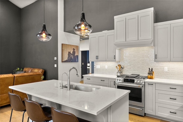 kitchen with a breakfast bar, sink, gas stove, decorative light fixtures, and an island with sink