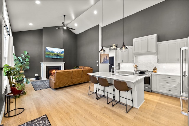 kitchen with high vaulted ceiling, decorative light fixtures, high end stove, a breakfast bar area, and a kitchen island with sink