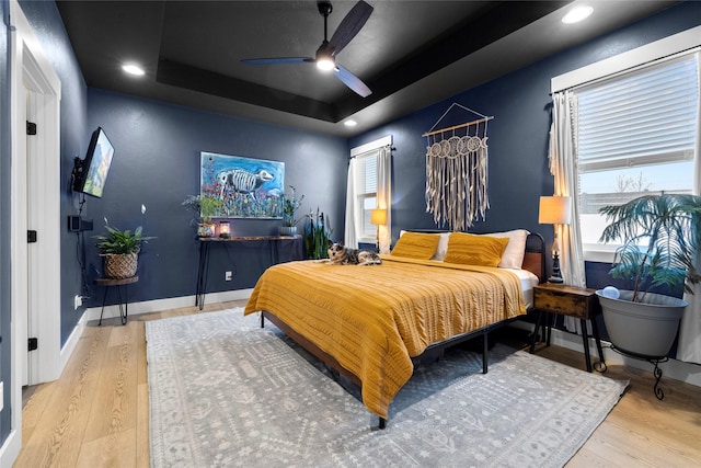 bedroom with ceiling fan, a tray ceiling, and light wood-type flooring