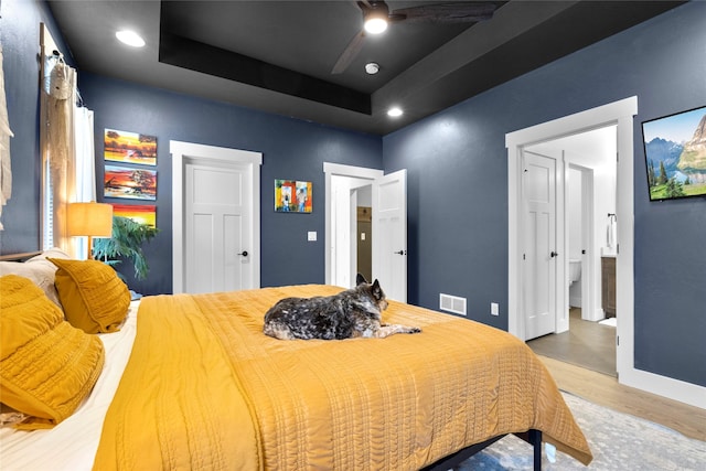 bedroom with a raised ceiling, wood-type flooring, and ceiling fan