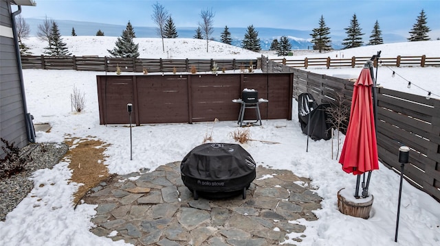 snow covered patio featuring a mountain view, a grill, and a fire pit