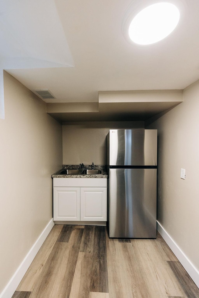 kitchen with stainless steel refrigerator, sink, white cabinets, dark stone counters, and light hardwood / wood-style flooring