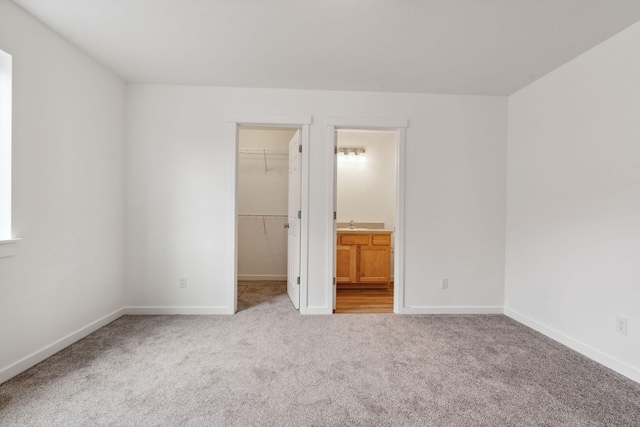 unfurnished bedroom with ensuite bathroom, a walk in closet, light colored carpet, and a closet