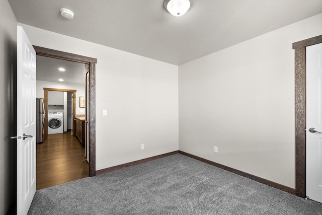 unfurnished bedroom featuring washer / dryer, freestanding refrigerator, dark carpet, and baseboards