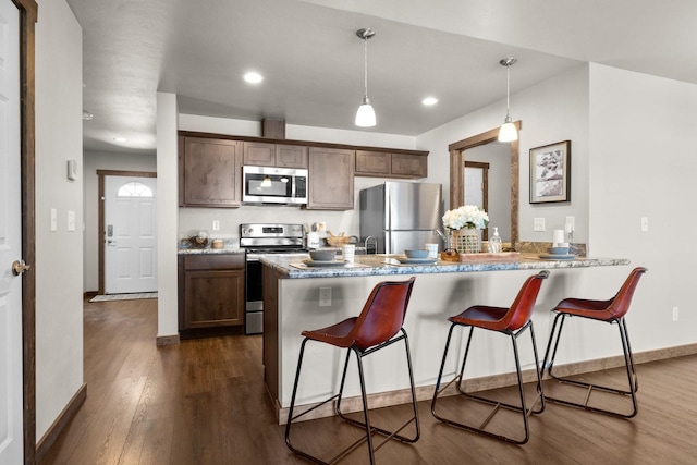 kitchen with appliances with stainless steel finishes, a peninsula, dark wood-style floors, a kitchen breakfast bar, and recessed lighting