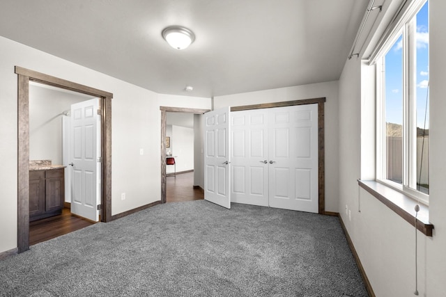 unfurnished bedroom with dark colored carpet, baseboards, multiple windows, and a closet