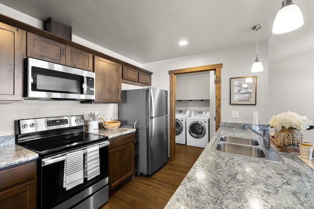 kitchen featuring appliances with stainless steel finishes, independent washer and dryer, a sink, dark wood-style floors, and hanging light fixtures
