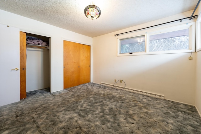 unfurnished bedroom featuring baseboard heating, dark carpet, a textured ceiling, and two closets