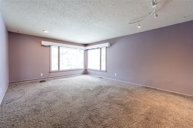 carpeted empty room featuring track lighting and a textured ceiling