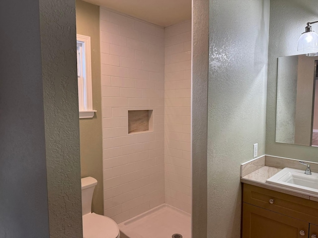 bathroom featuring vanity, a tile shower, and toilet