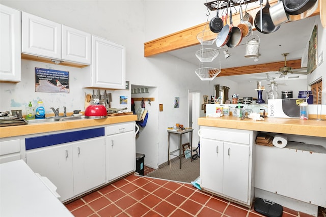 kitchen with beamed ceiling, tile patterned floors, sink, and white cabinets