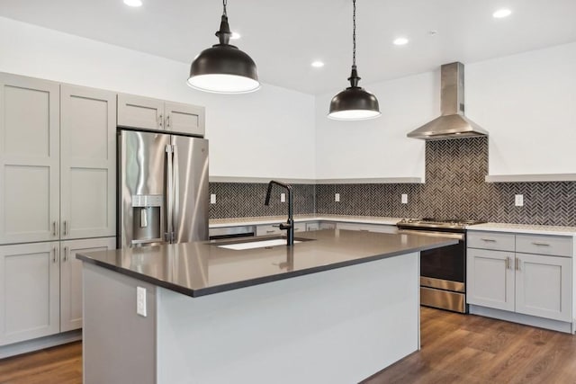 kitchen featuring decorative light fixtures, sink, a kitchen island with sink, stainless steel appliances, and wall chimney exhaust hood