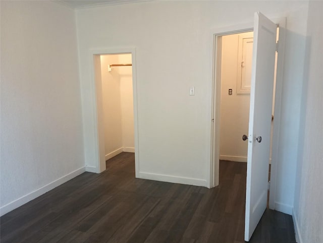 unfurnished bedroom featuring a walk in closet, dark wood finished floors, and baseboards